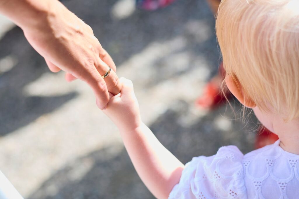 Blonde child holding parent's hand outdoors, symbolizing love and protection.